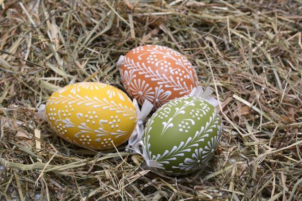 Three pastel Easter eggs with white decorations sit in straw