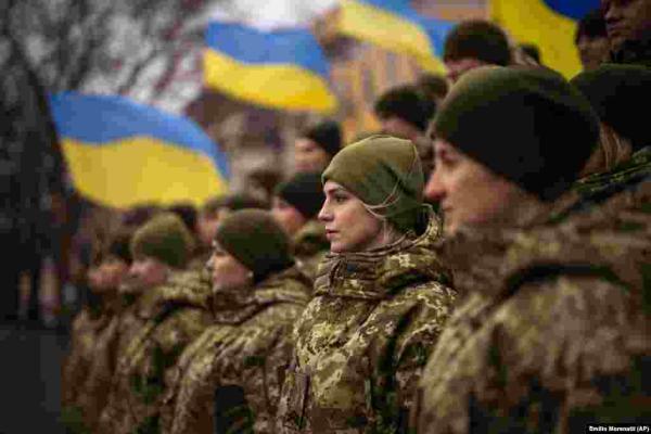 Female Ukrainian solders standing next to the Ukrainian flag