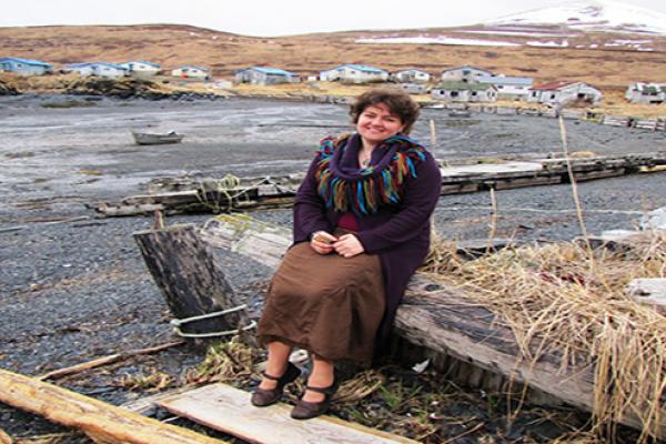 Woman sitting on a piece of timber with a village and mountains far away in background