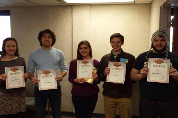 Five students standing in row each holding a certificate