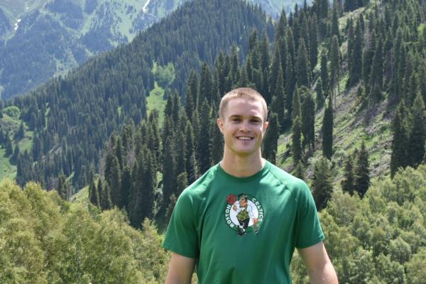 Young man standing and smiling with moutains and forest in the background