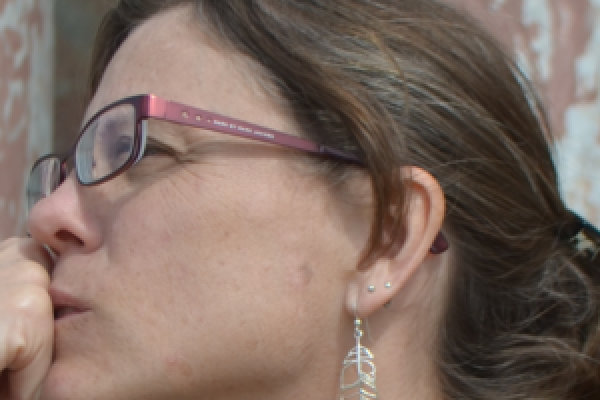 A side profile of a woman's head wearing glasses and dangling earrings