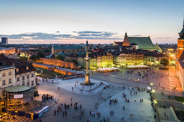 Image of a city taken from above in the evening, showing a square, brick buildings, and illuminated lights