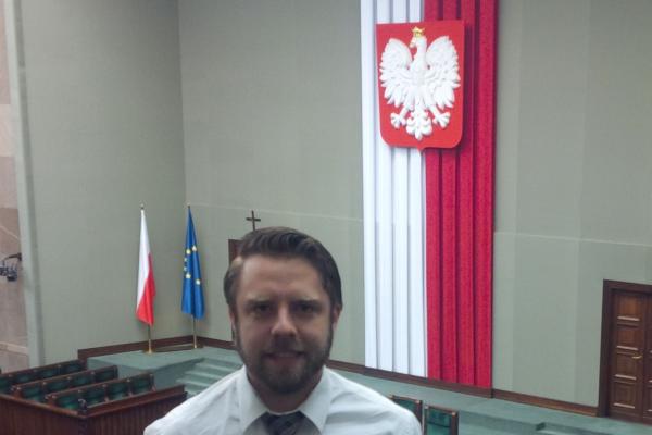 A man standing overlooking a gallery with a flag hanging in background.